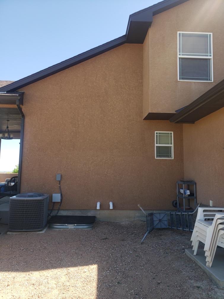 The corner of a two-story tan stucco house, sound and even to the ground.