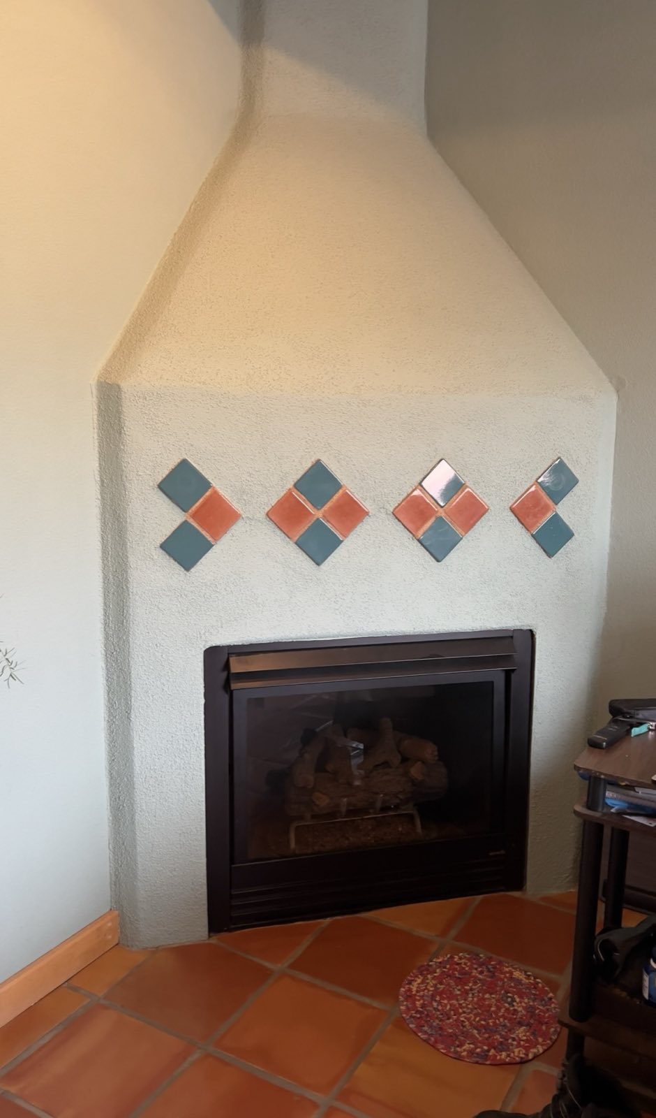 A Kiva fireplace before the work, with rows of diamond-set decorative tiles across the face.