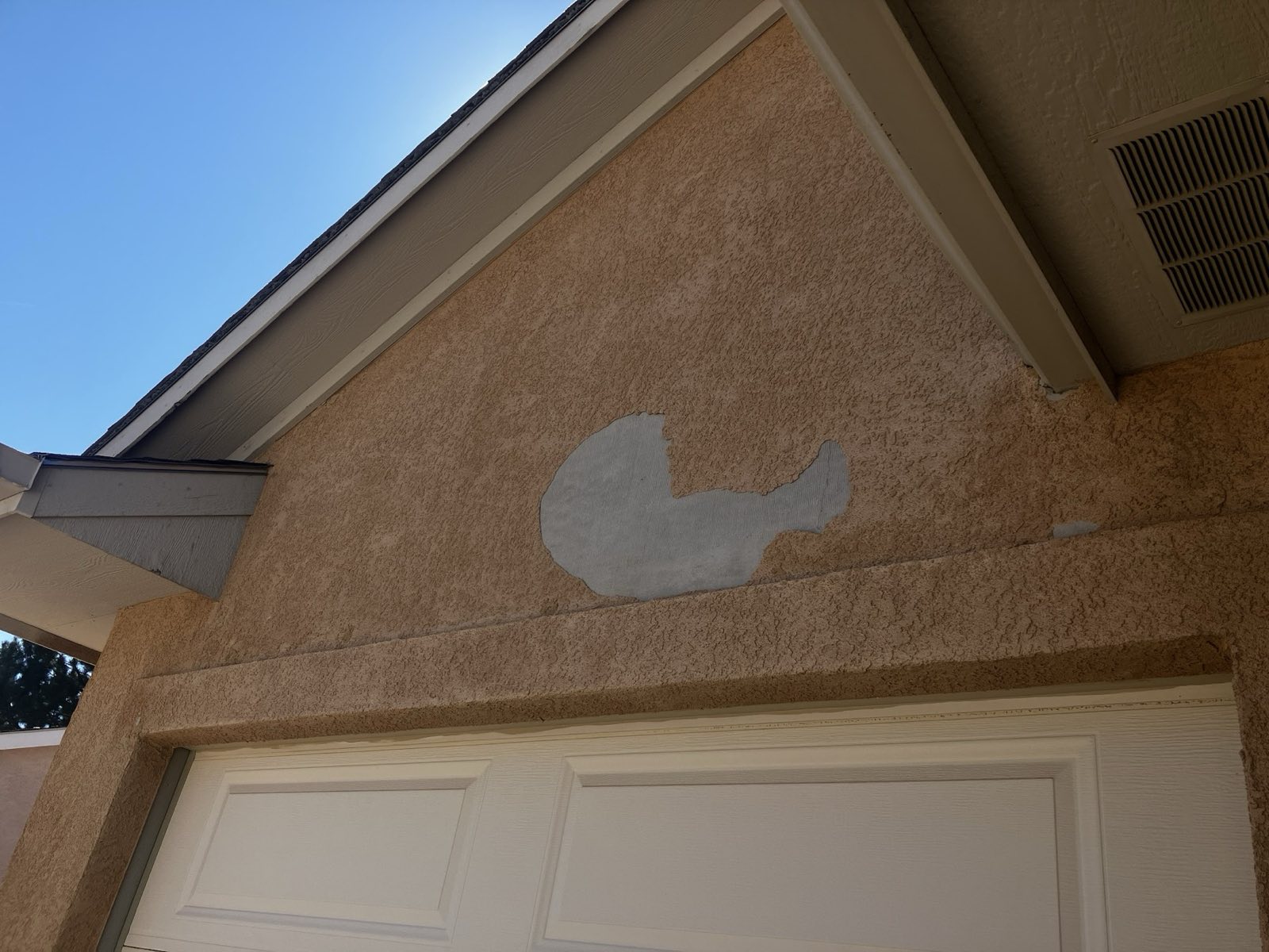 A patched area on a tan stucco wall above a garage door, still reading lighter than the wall around it.