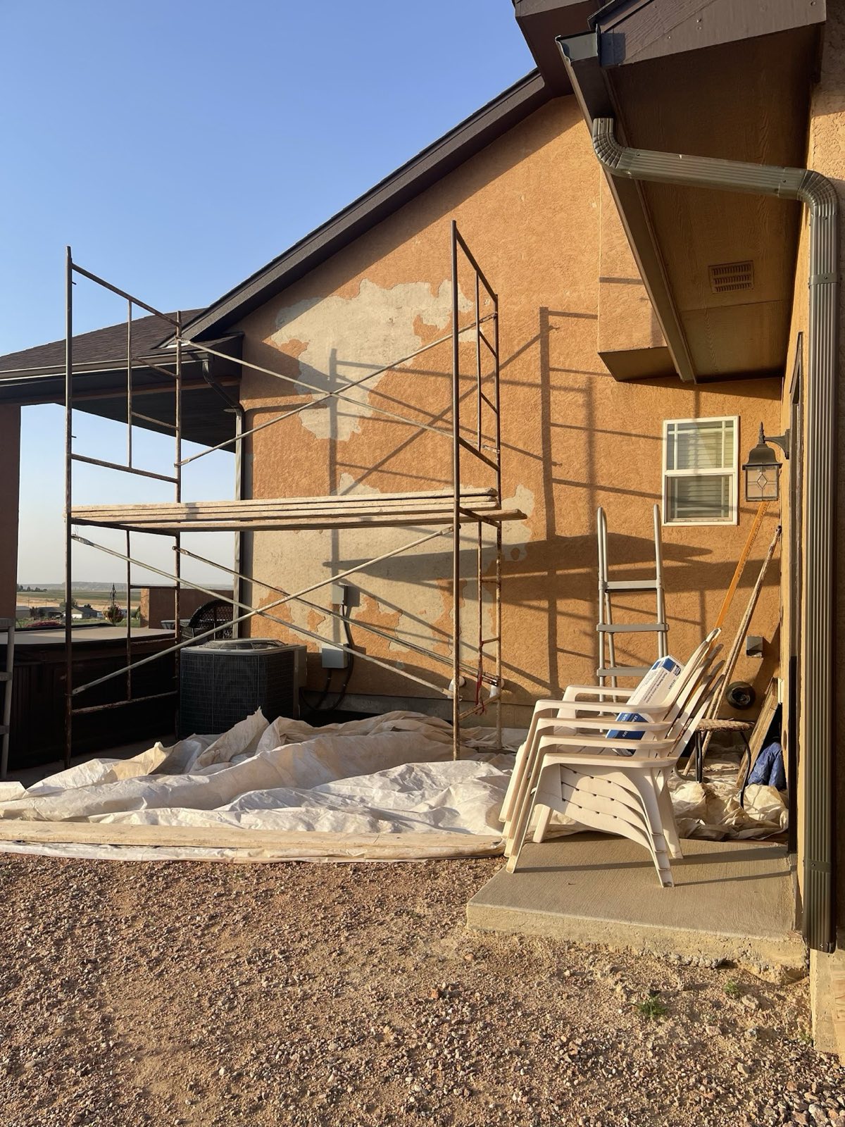 Scaffolding standing against a two-story house part-way through its tan stucco coat.
